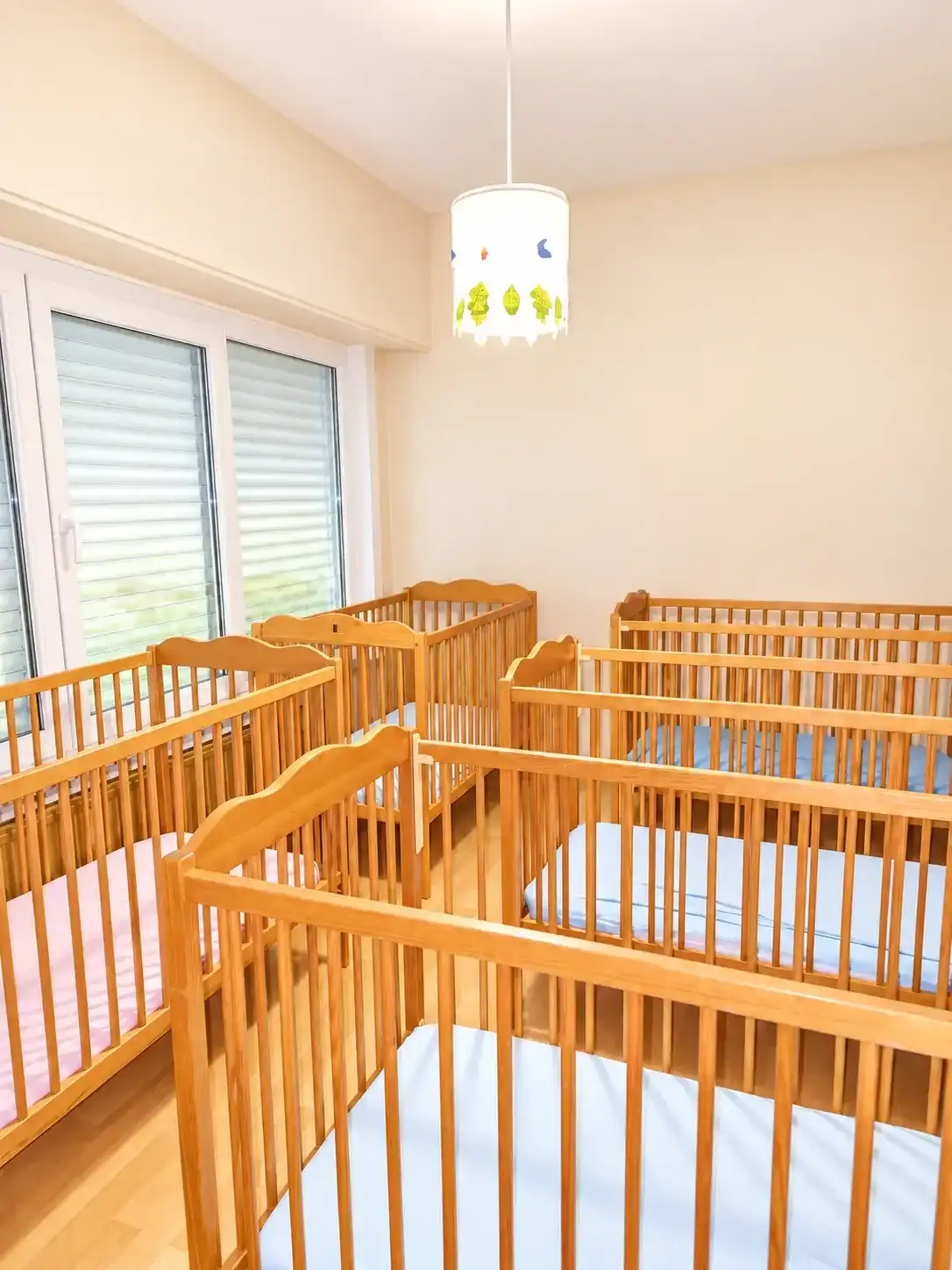 Kindercrèche met houten kinderbedjes en grote ramen voor natuurlijk licht.